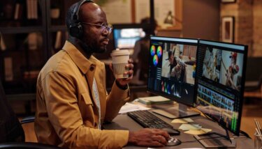 Person working at computer screens with headphones and a coffee